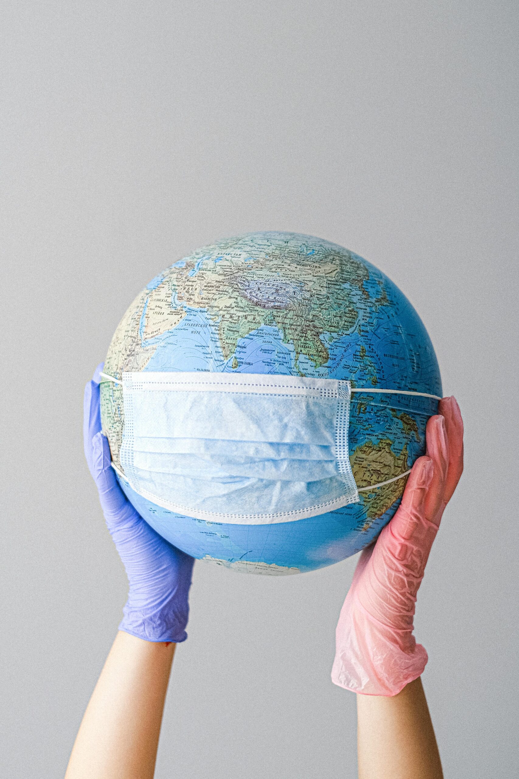 Hands With Latex Gloves Holding a Globe with a Face Mask